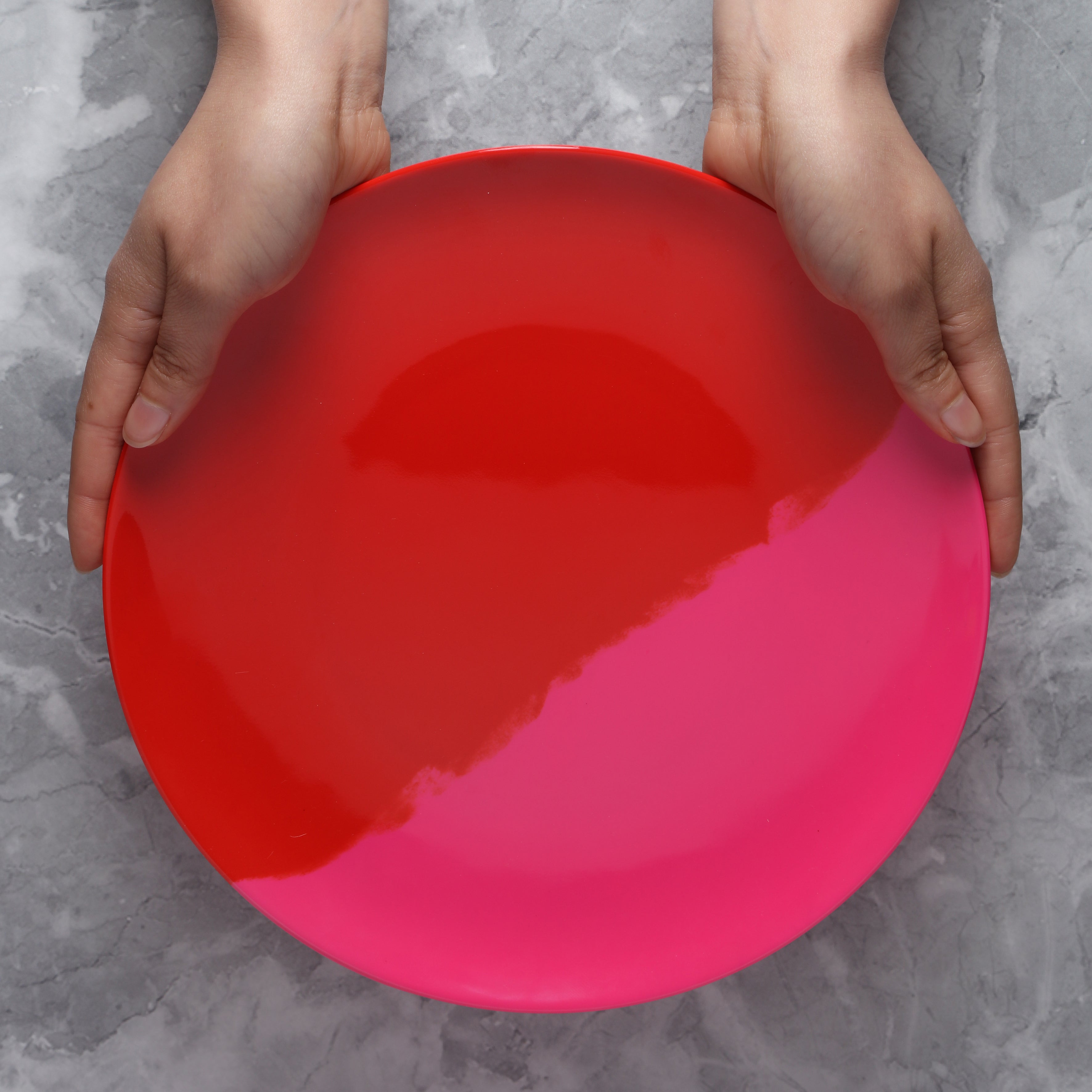 Person holding a red and pink Melamine plate on a gray surface