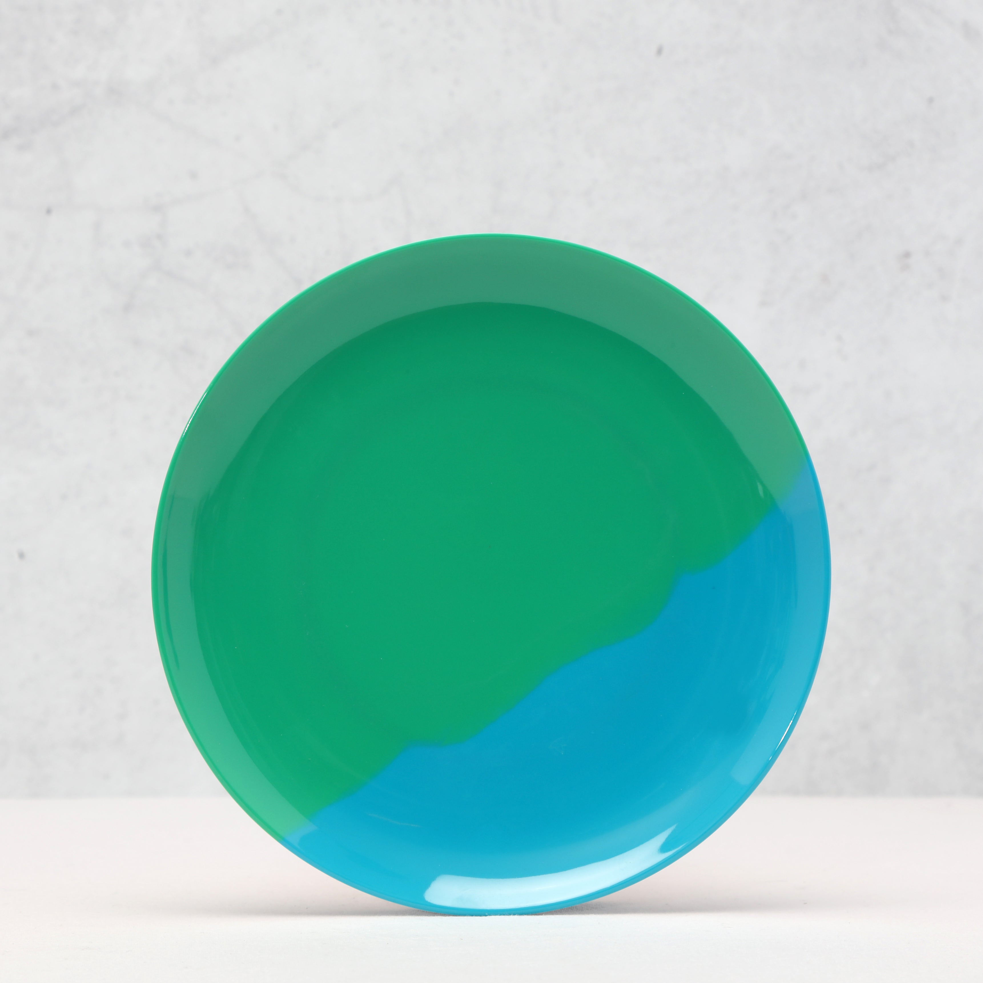 Green and blue round melamine plate on a textured white background