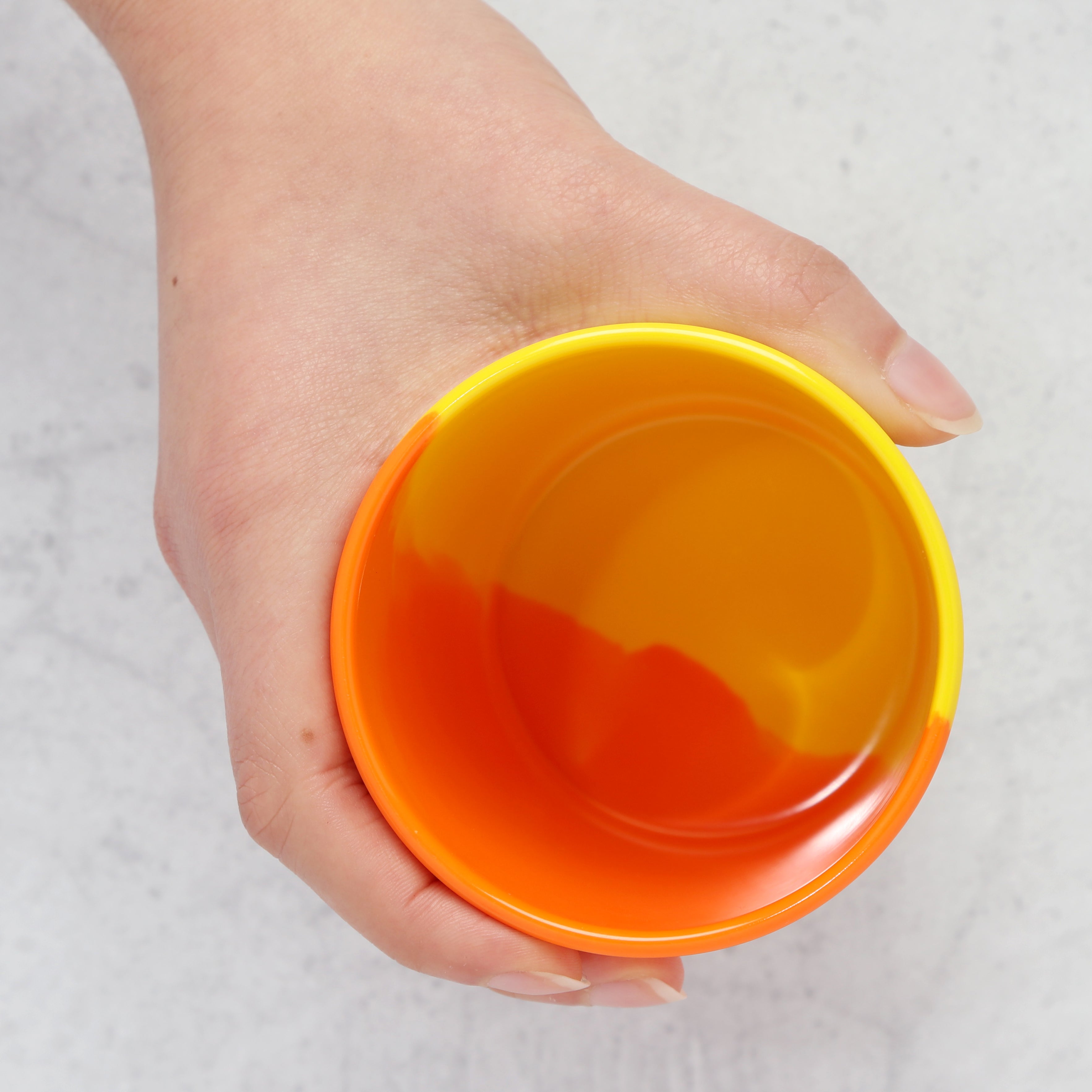 Hand holding an orange and yellow melamine tumbler against a light gray background