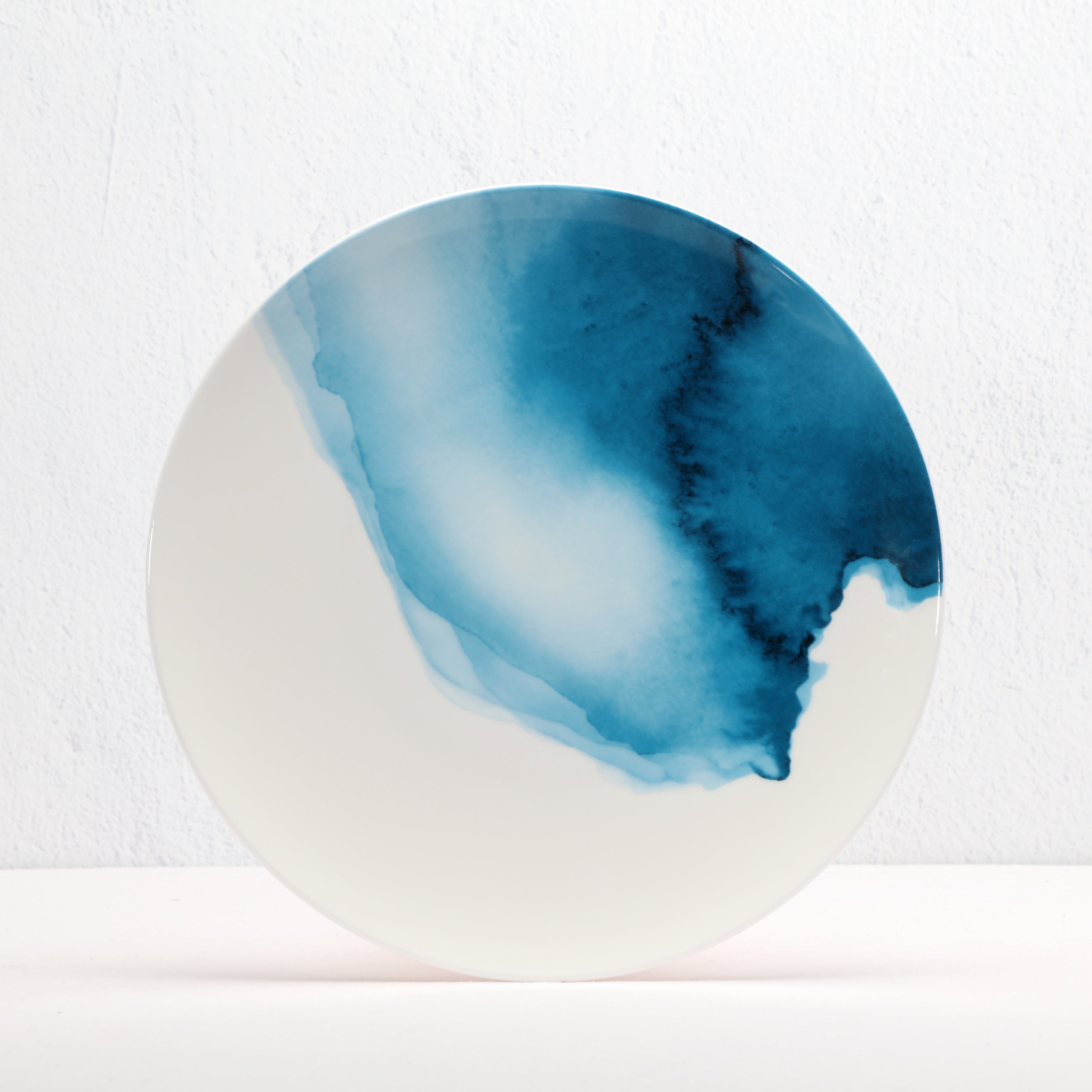 Round bone china ceramic plate with blue watercolor design on a white background