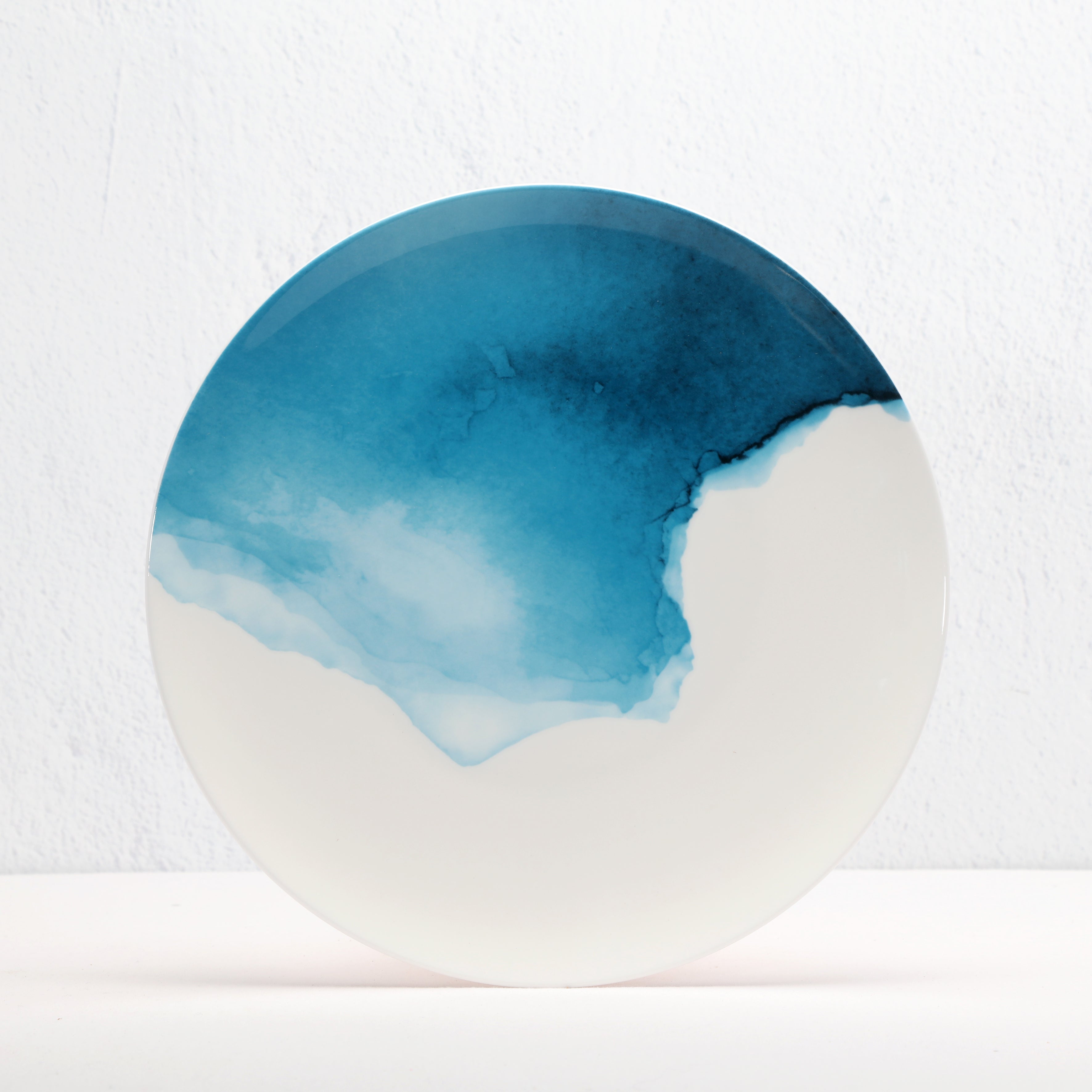 Round bone china ceramic plate with blue and white gwatercolour design on a white background