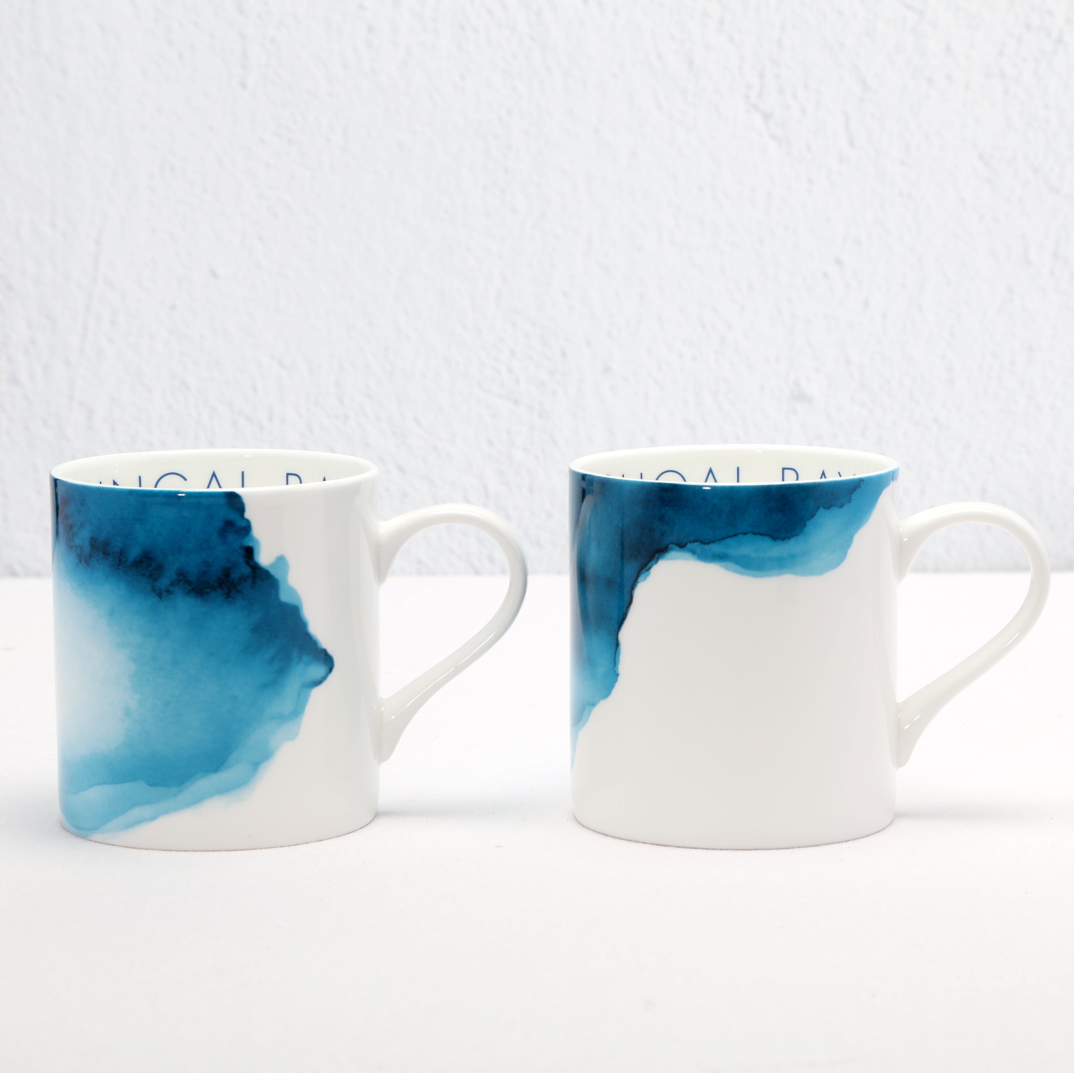 Two white mugs with blue watercolour designs on a white background