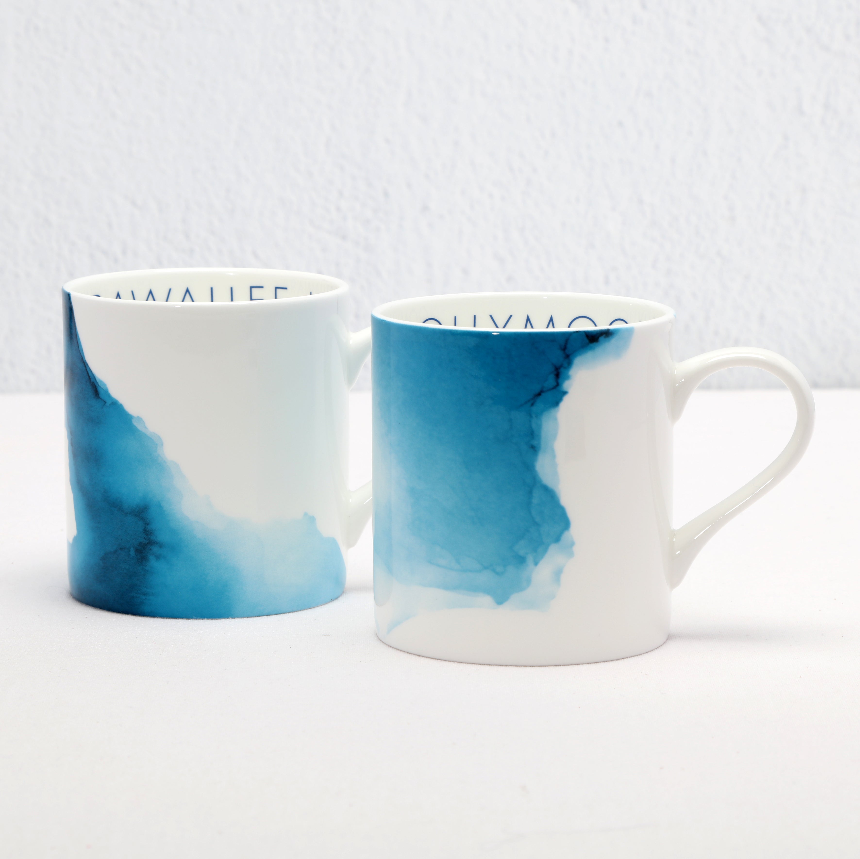 Two bone china mugs with blue and white watercolour designs on a light gray background