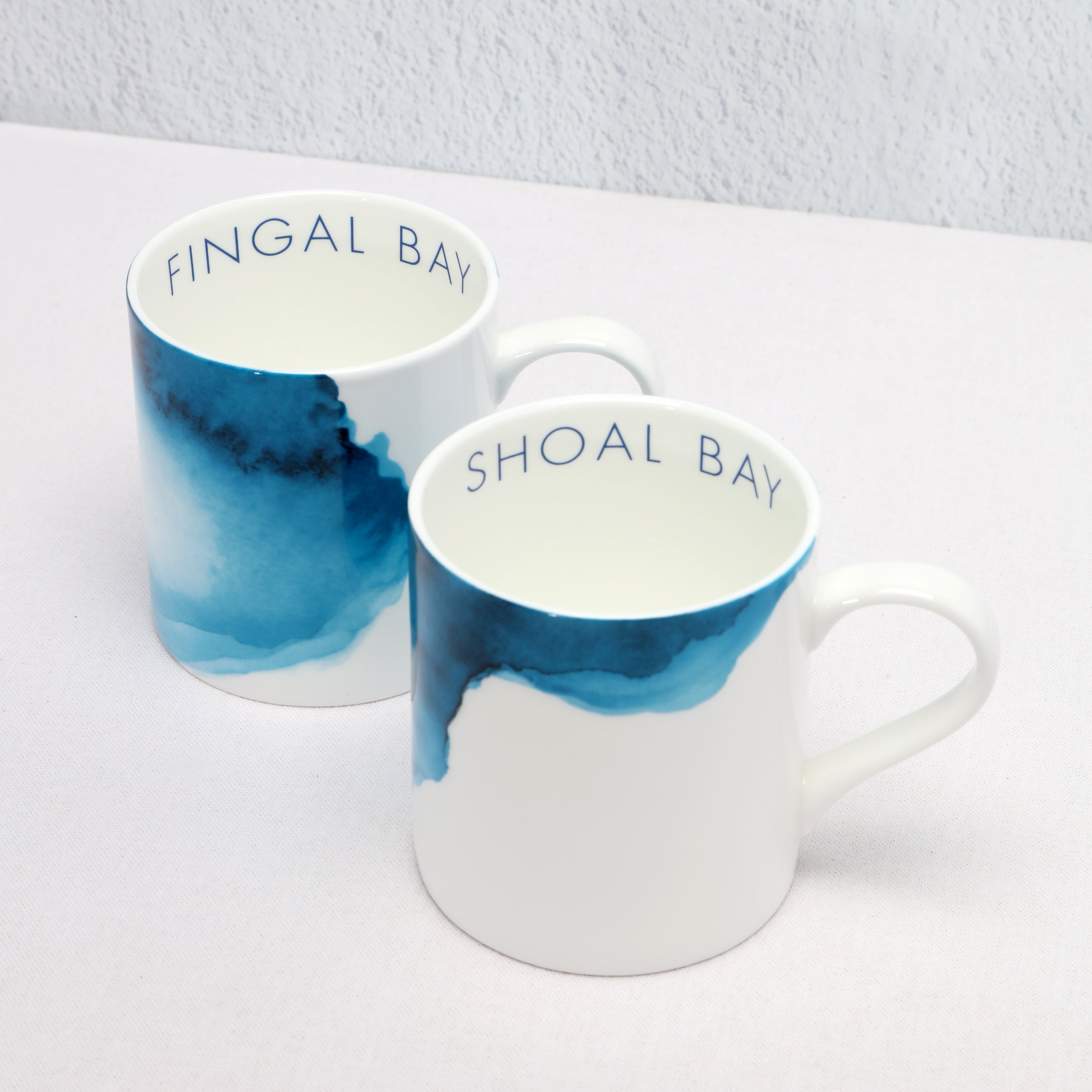 Two mugs with blue watercolor design and text on a white surface at angle