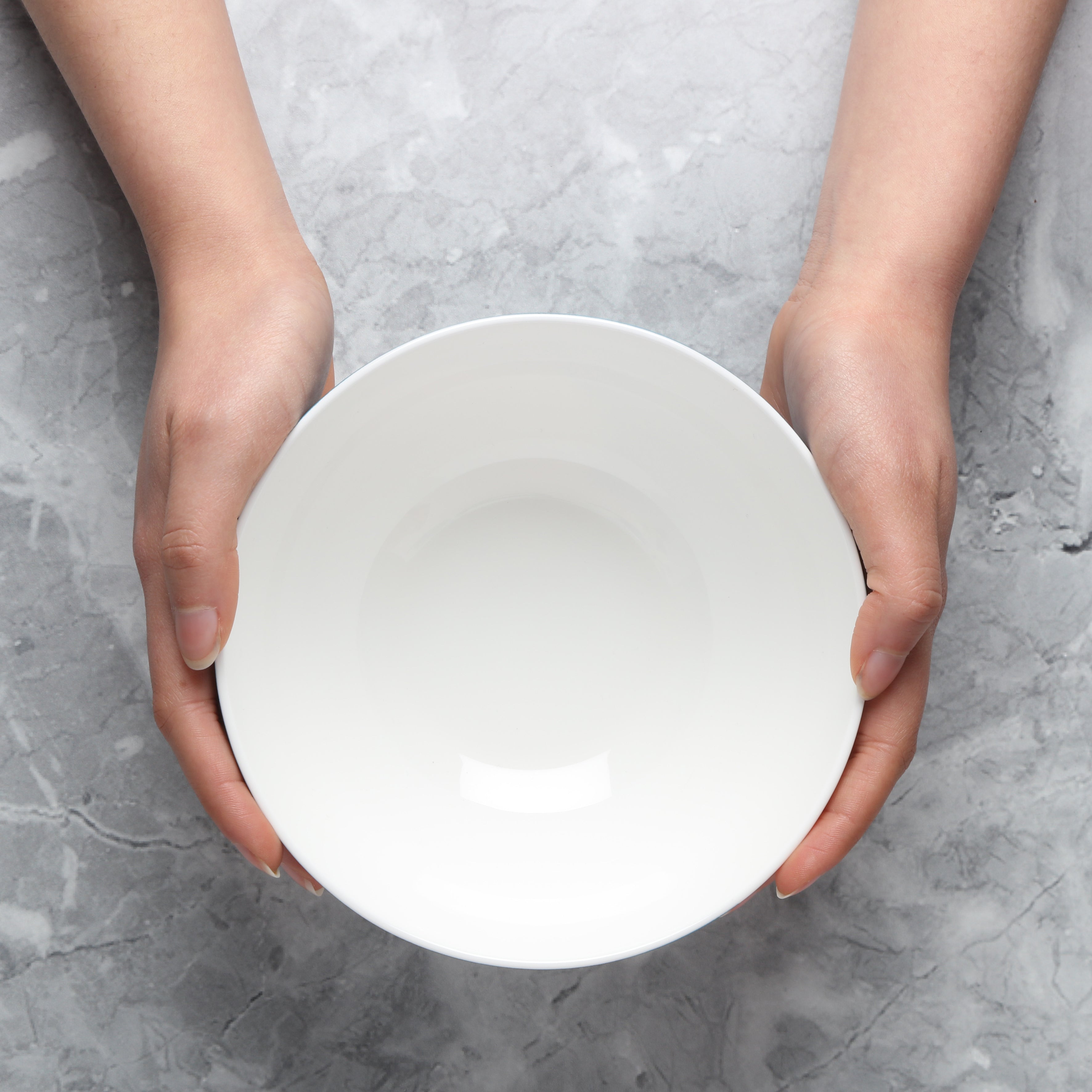 White Pasta bowl held by hands on a gray concrete background