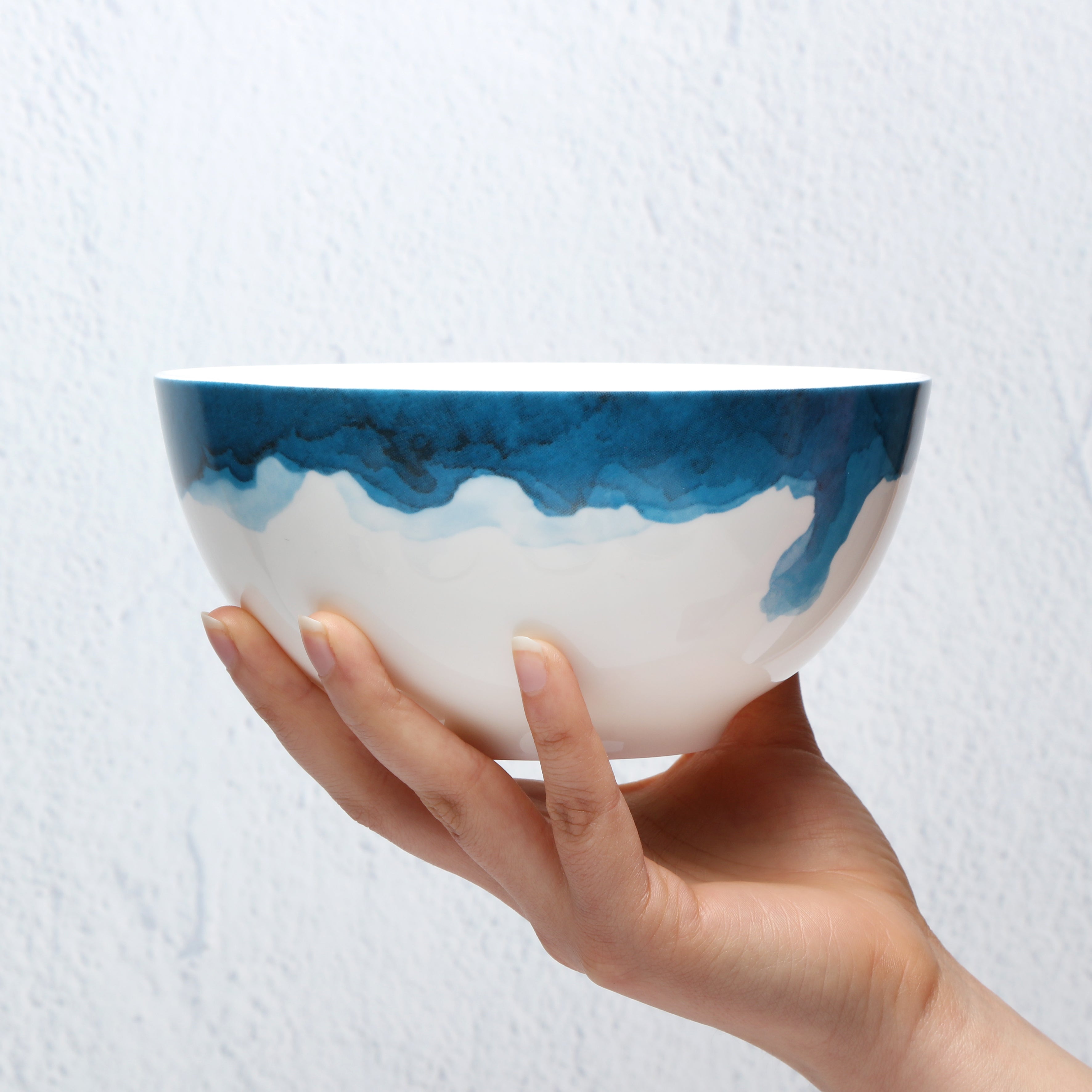 Hand holding a Bone China ceramic bowl with blue and white design against a light background