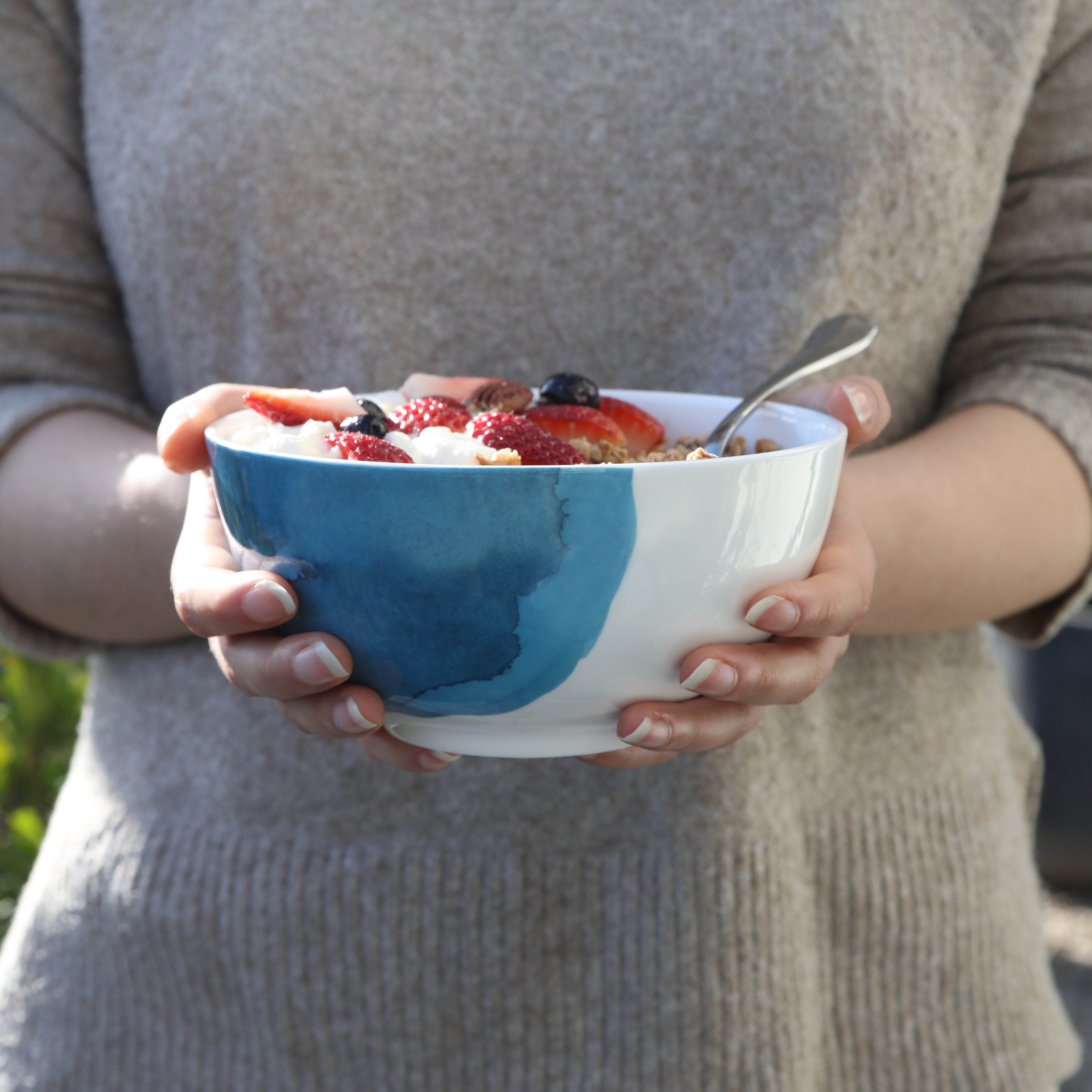 Person holding a bowl of cereal with berries outdoors