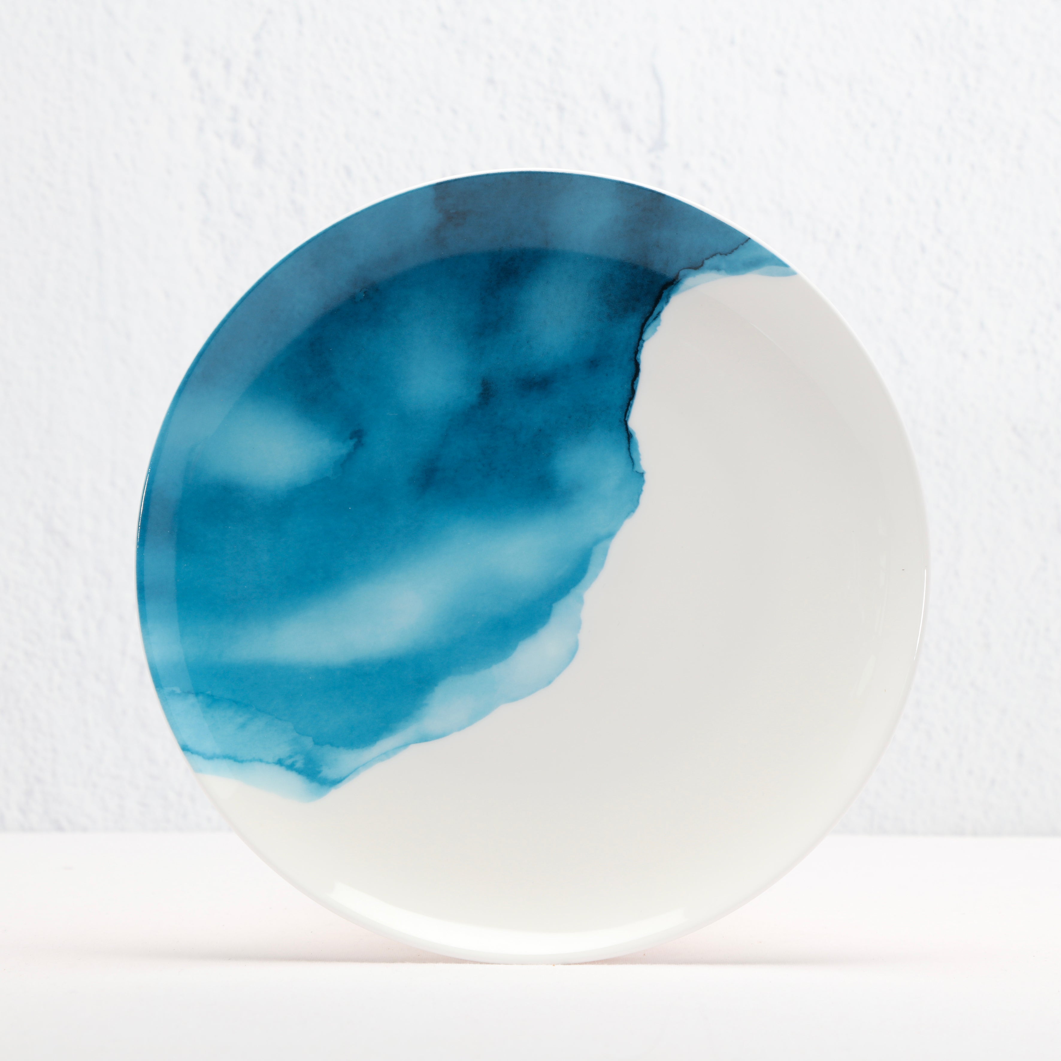 Round bone china ceramic plate with blue watercolour design on a white background