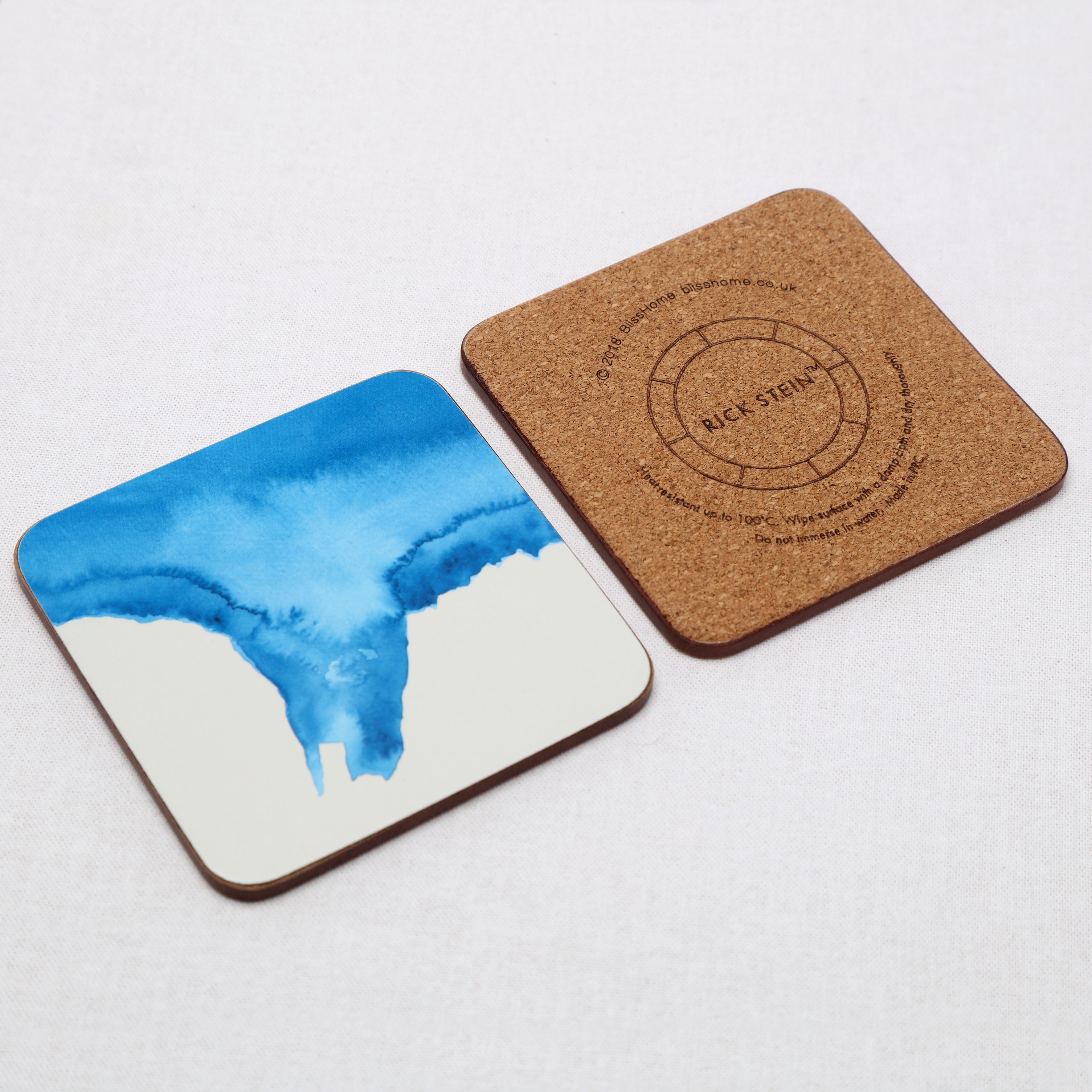 Two coasters, one with a blue watercolor design and the other with a cork texture and branding, on a light gray background.