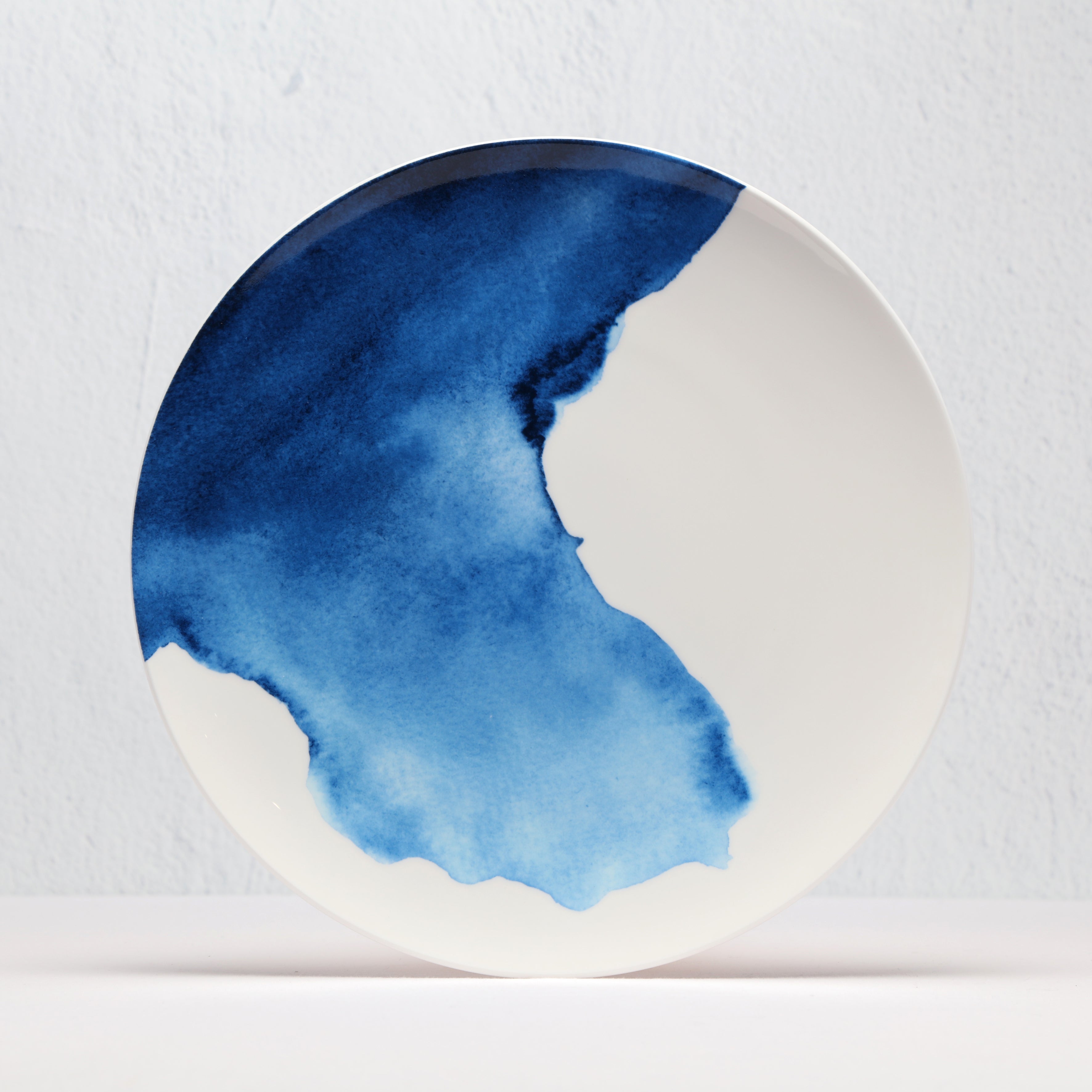 Round ceramic bone china plate with blue watercolor design on a light gray background