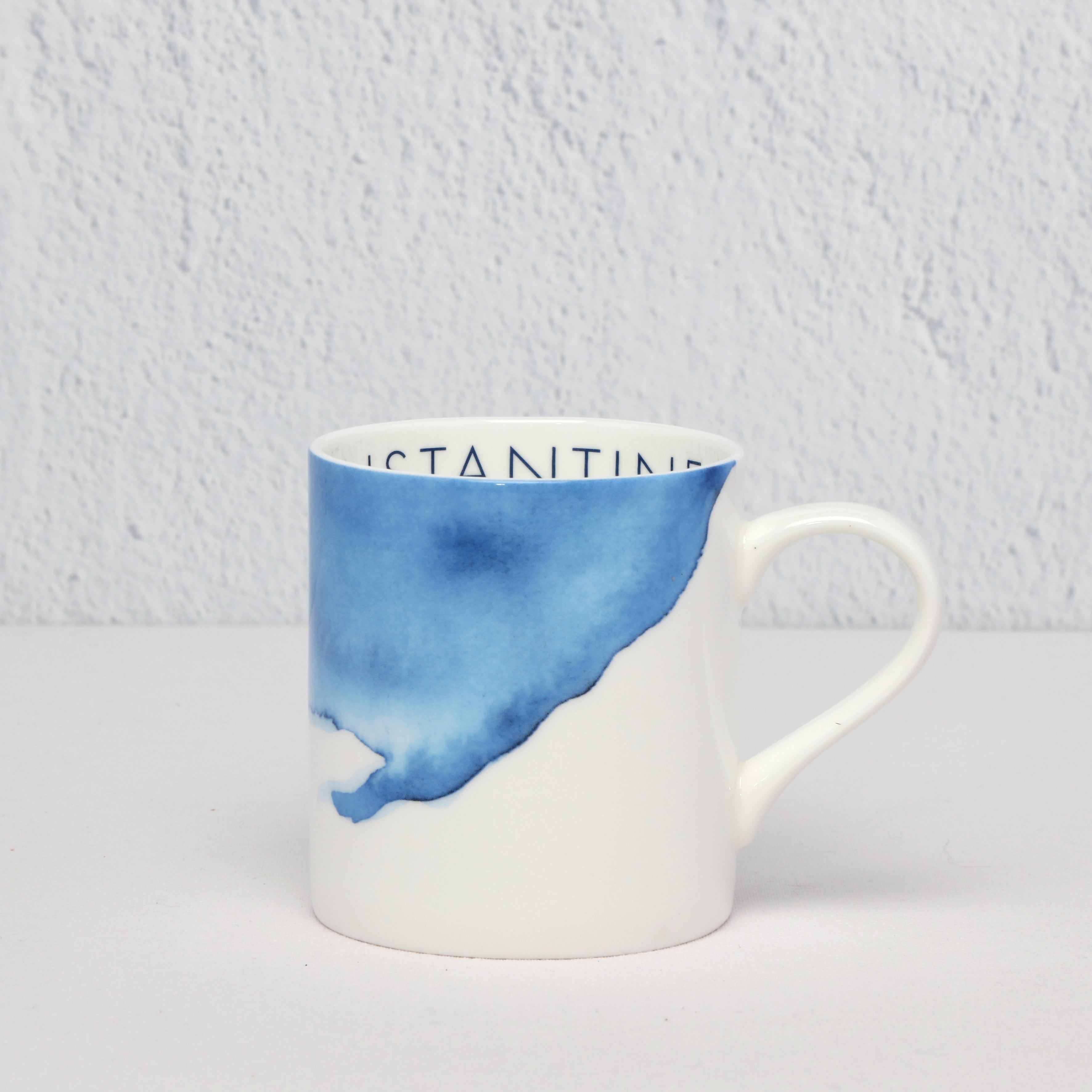 White mug with blue watercolor design and 'Constantine Bay ' text on a light gray background