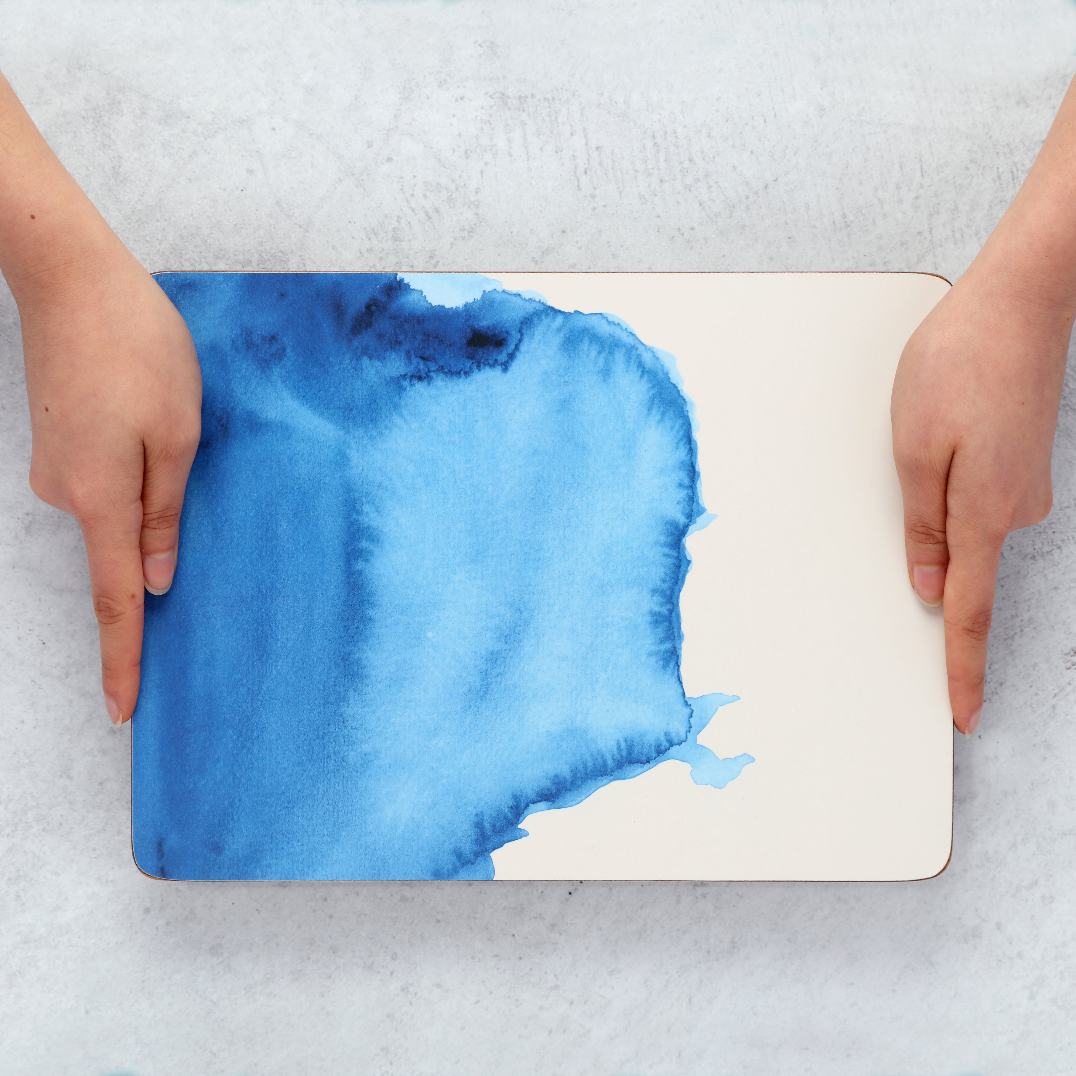 Person holding a placemat with blue watercolor design on a textured surface