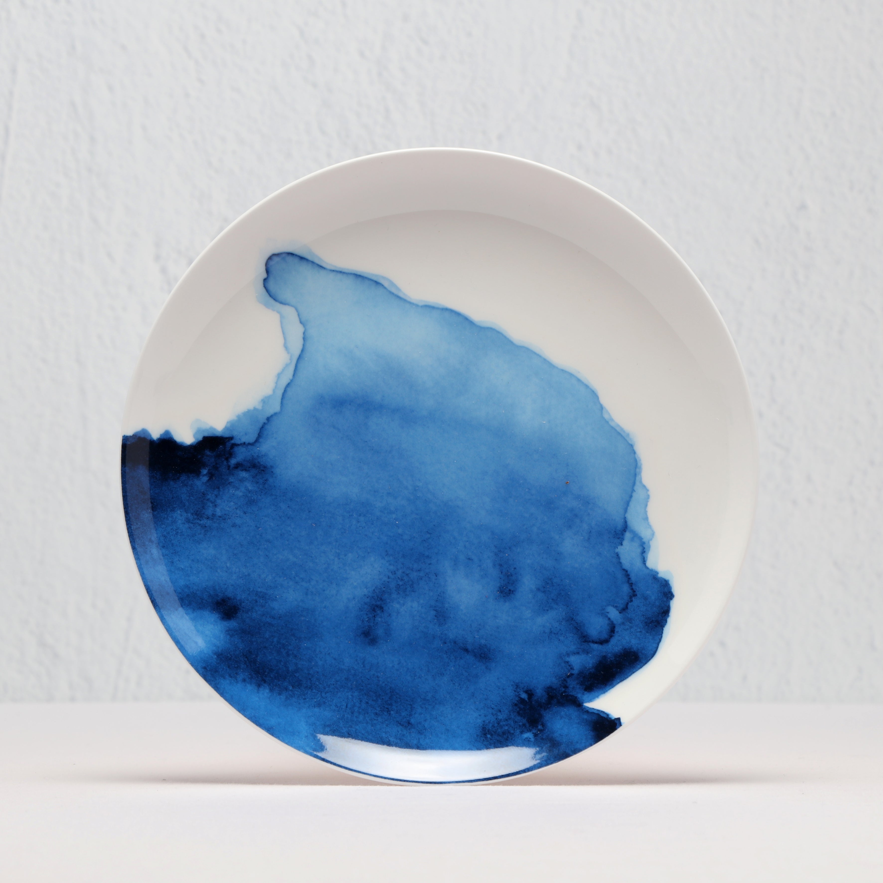 White bone china plate with blue watercolour design on a light gray background