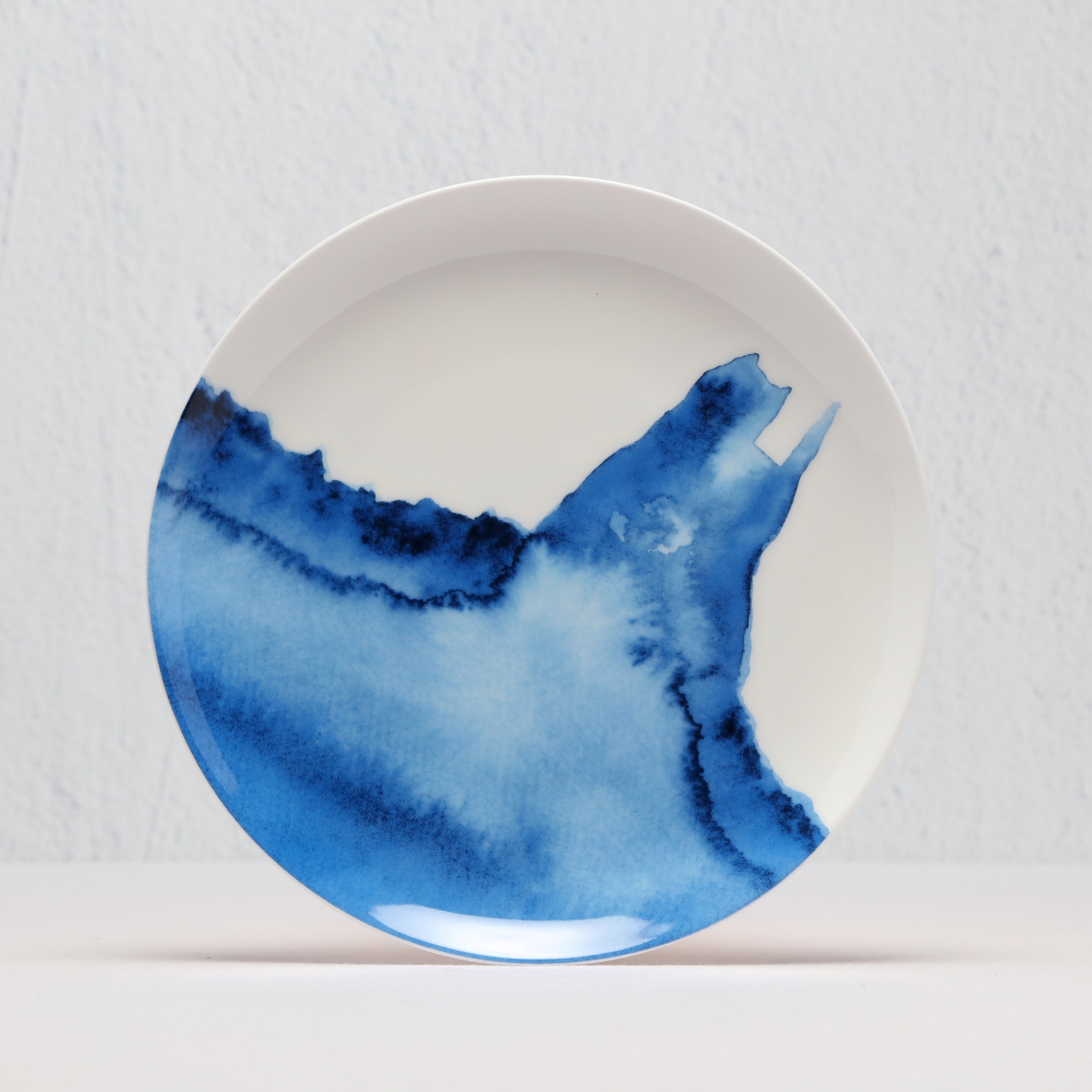 White side plate with blue watercolour design on a light gray background
