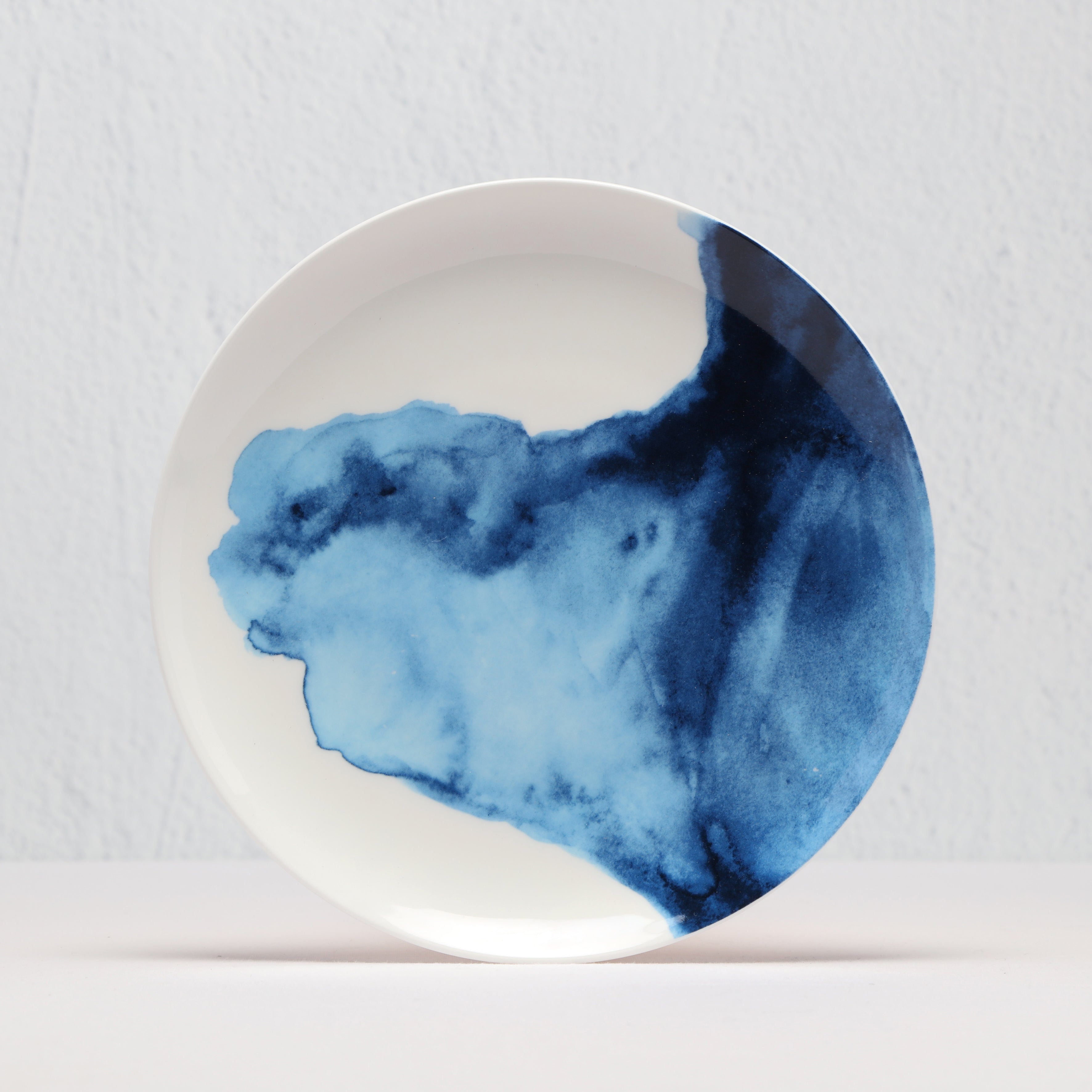 Round side plate with blue watercolour design on a light gray background