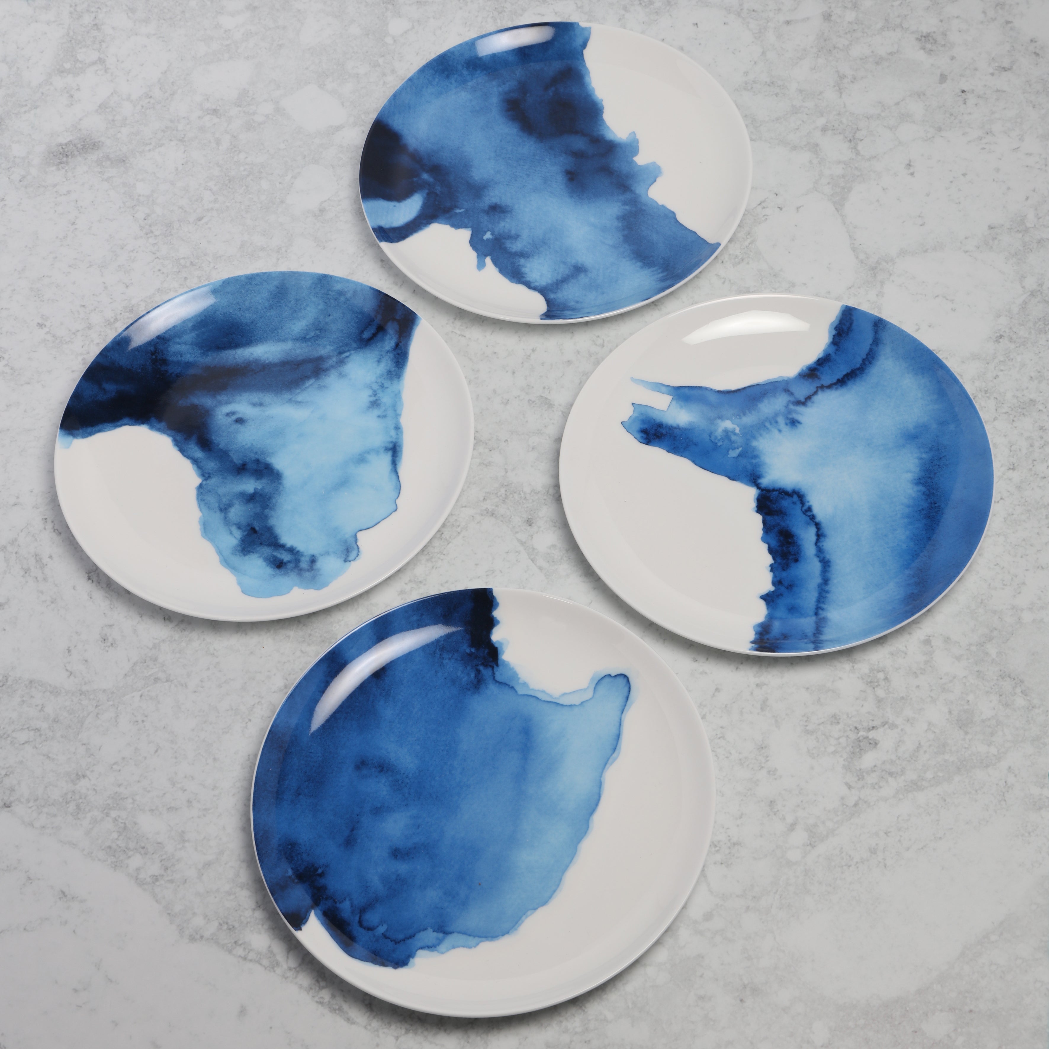 Four ceramic side plates with blue watercolour designs on a gray surface