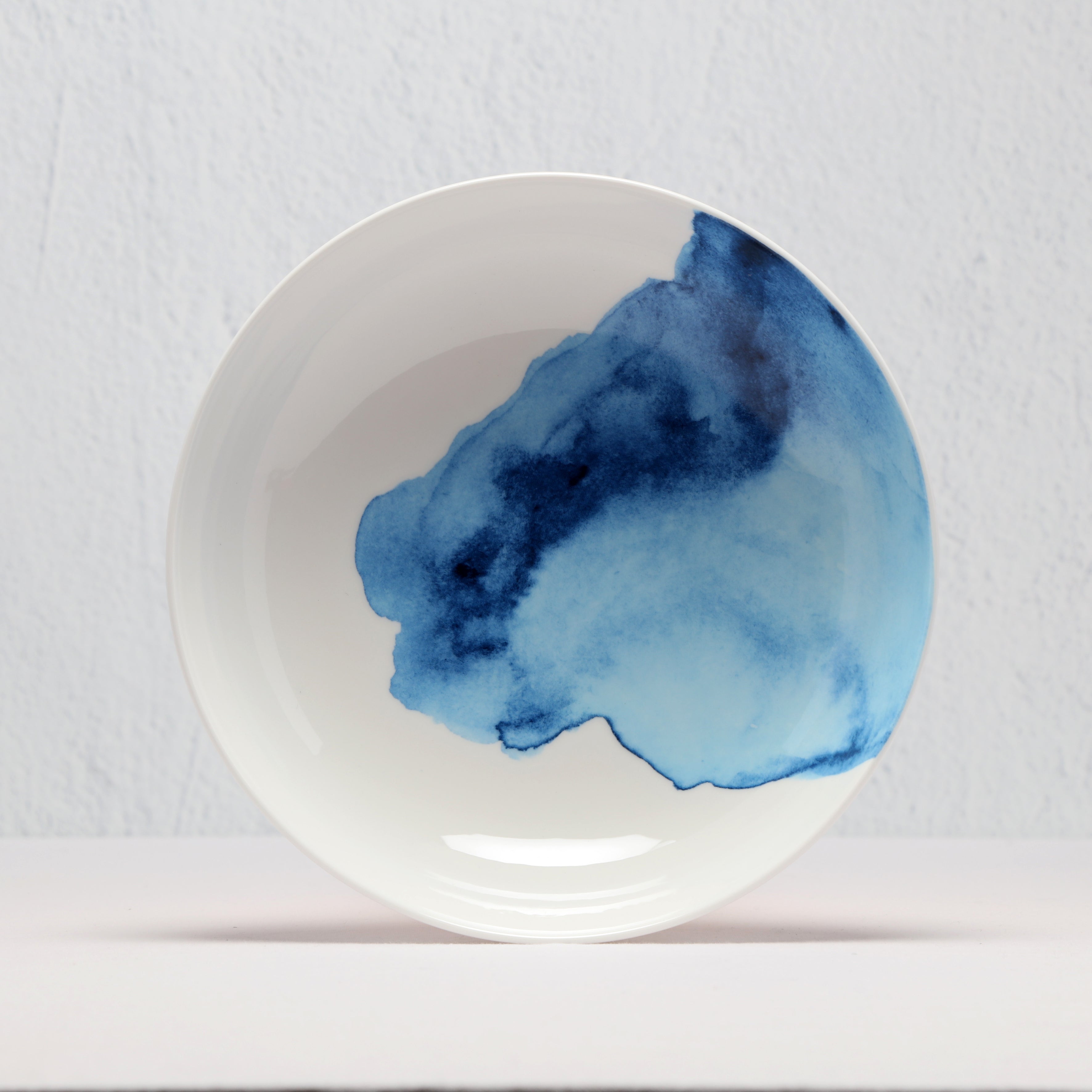 White supper bowl with a blue watercolor design on a light gray background