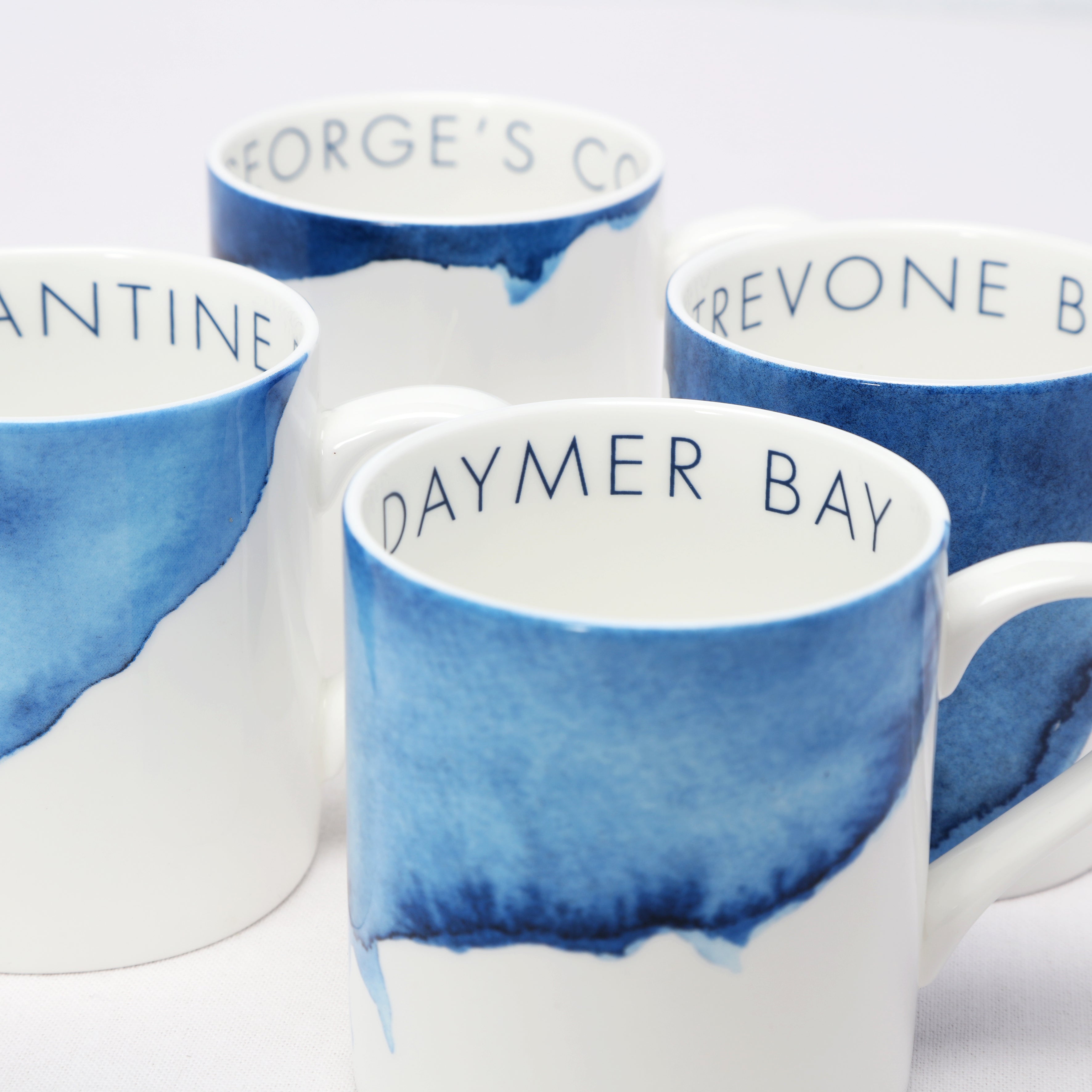 Set of four bone china mugs with blue and white design and text on a white background