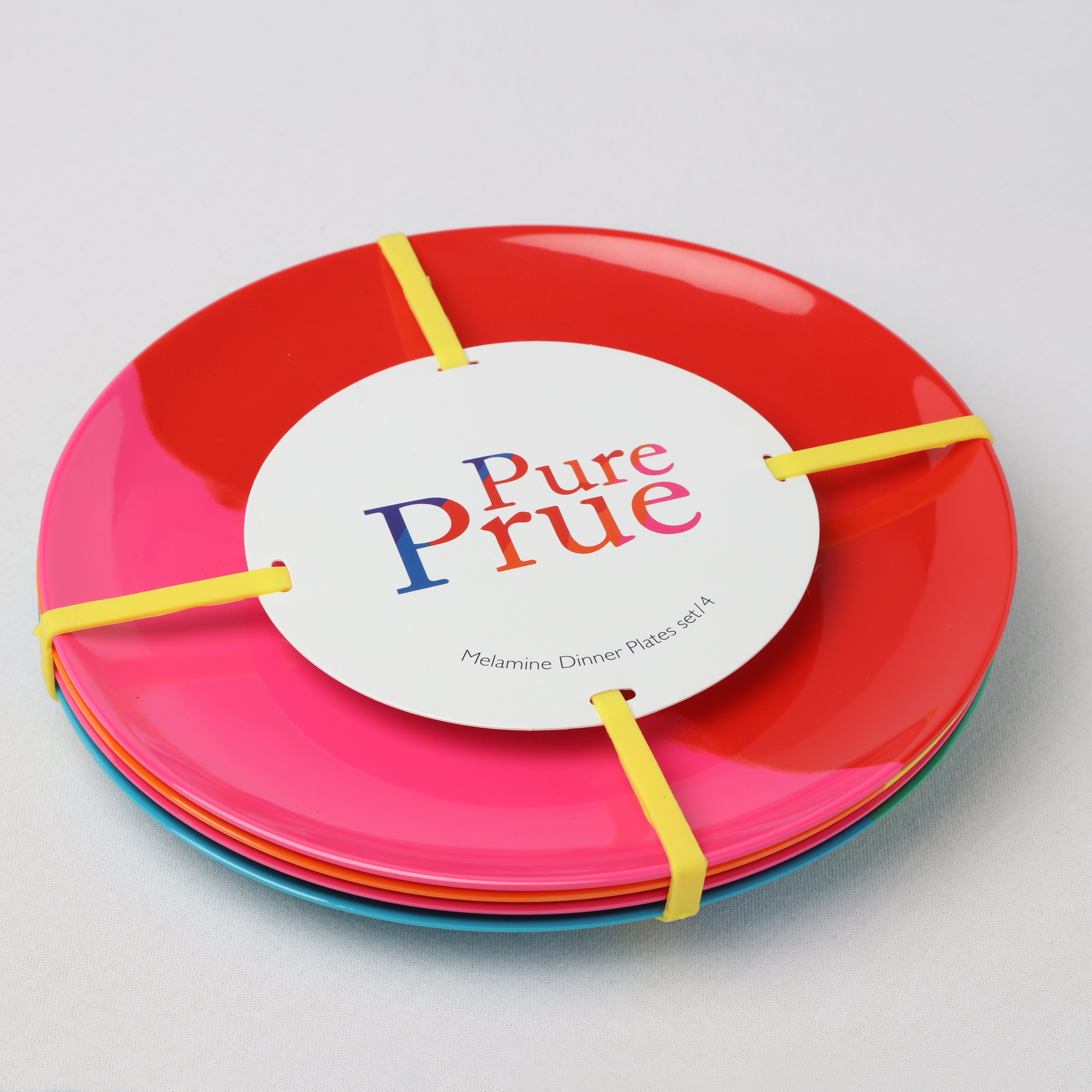 Stack of colorful melamine dinner plates with 'Pure Prue' label on a light gray background