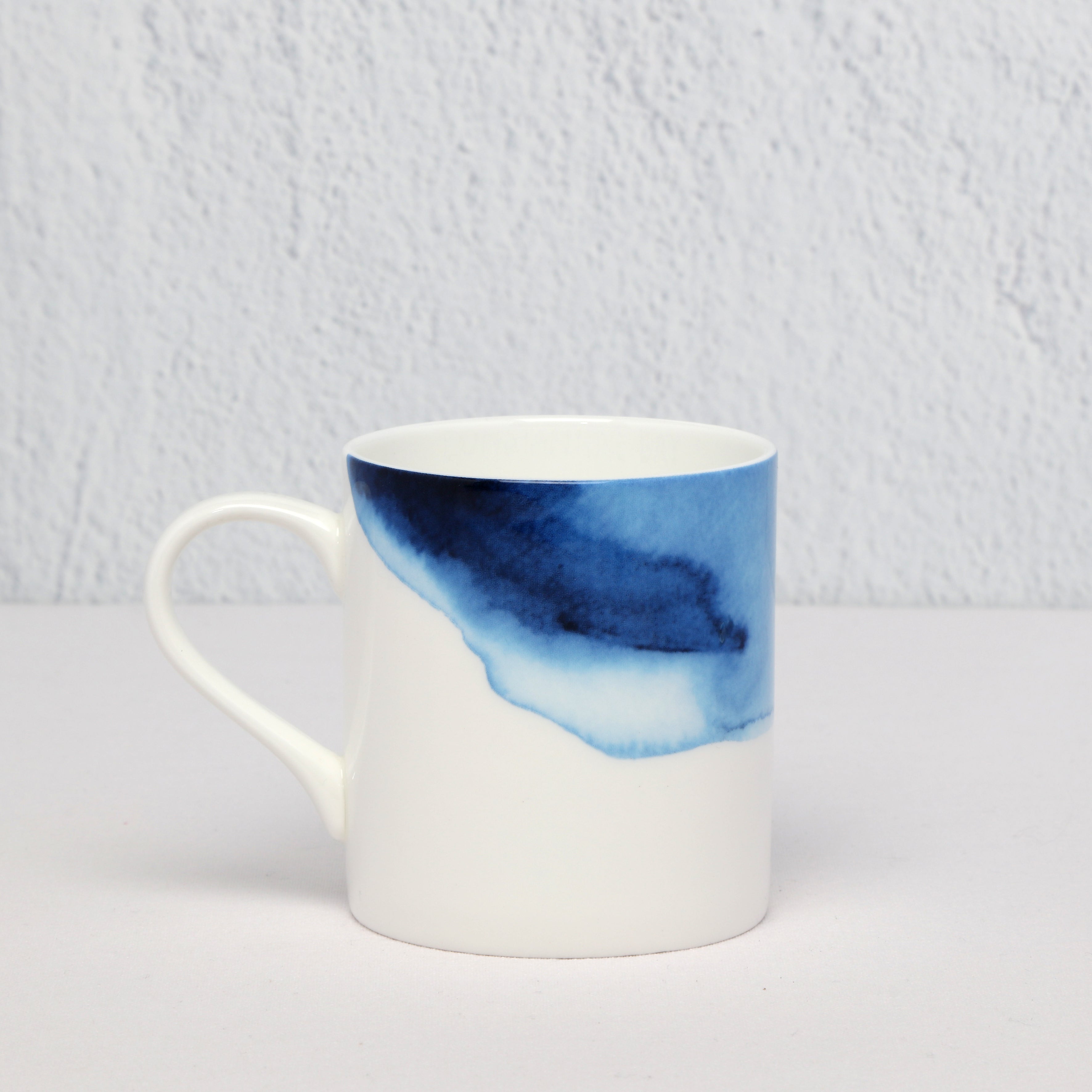 White bone China mug with blue watercolor design on a light gray background