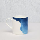 White mug with blue watercolor design on a light gray background
